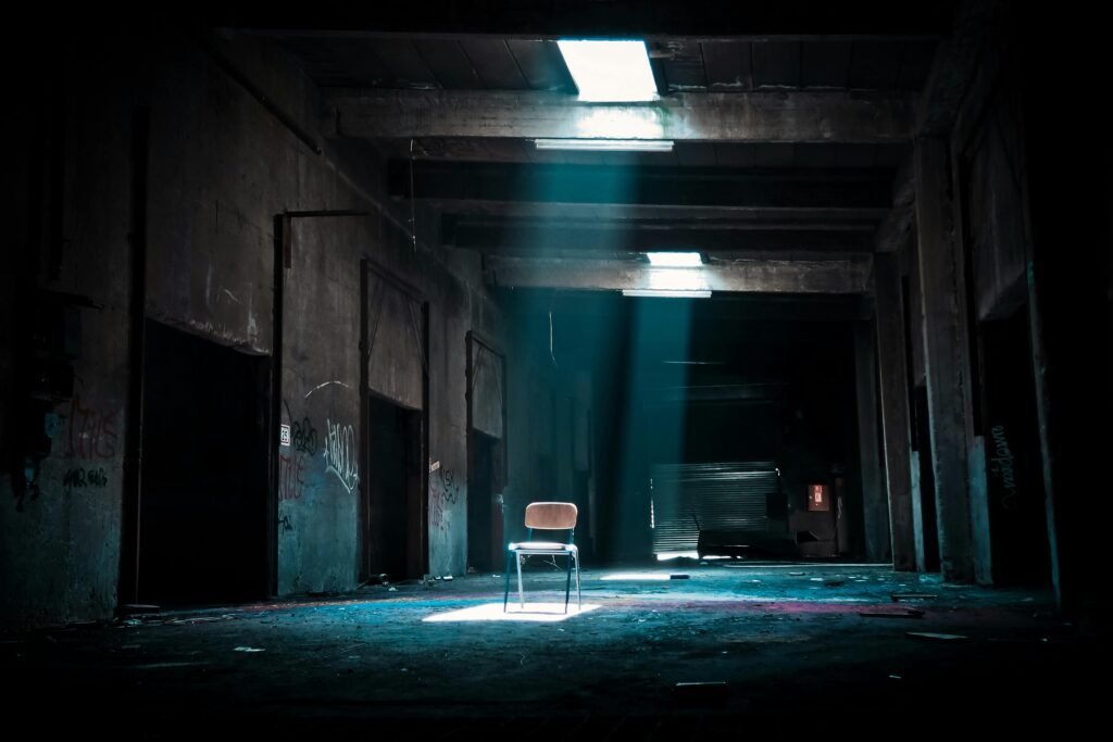 Eerie abandoned warehouse with a solitary chair illuminated by sunlight, evoking mystery.