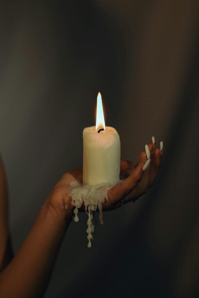 A vivid close-up of a hand holding a burning candle against a dark background.