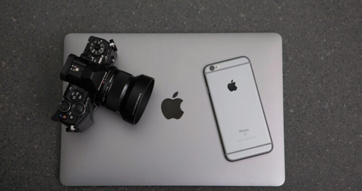 High-angle shot of DSLR camera, MacBook, and iPhone on textured surface, showcasing modern technology essentials.