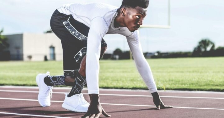 Focused athlete in starting position on a sunny track field, ready to sprint.