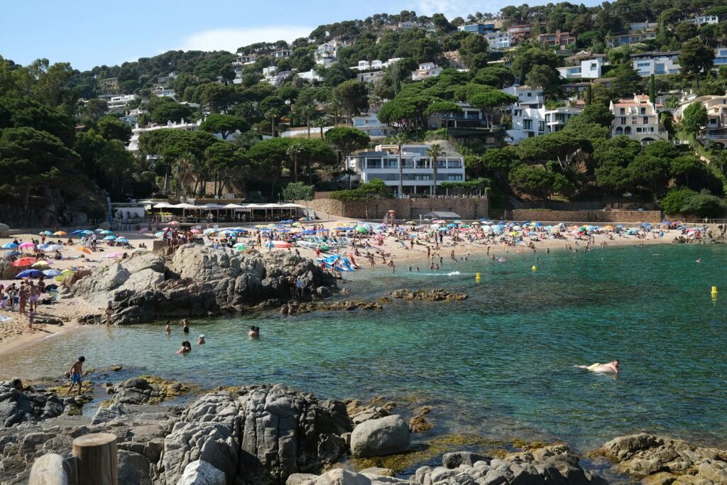 Crowded summer beach scene with turquoise waters and houses on Costa Brava.